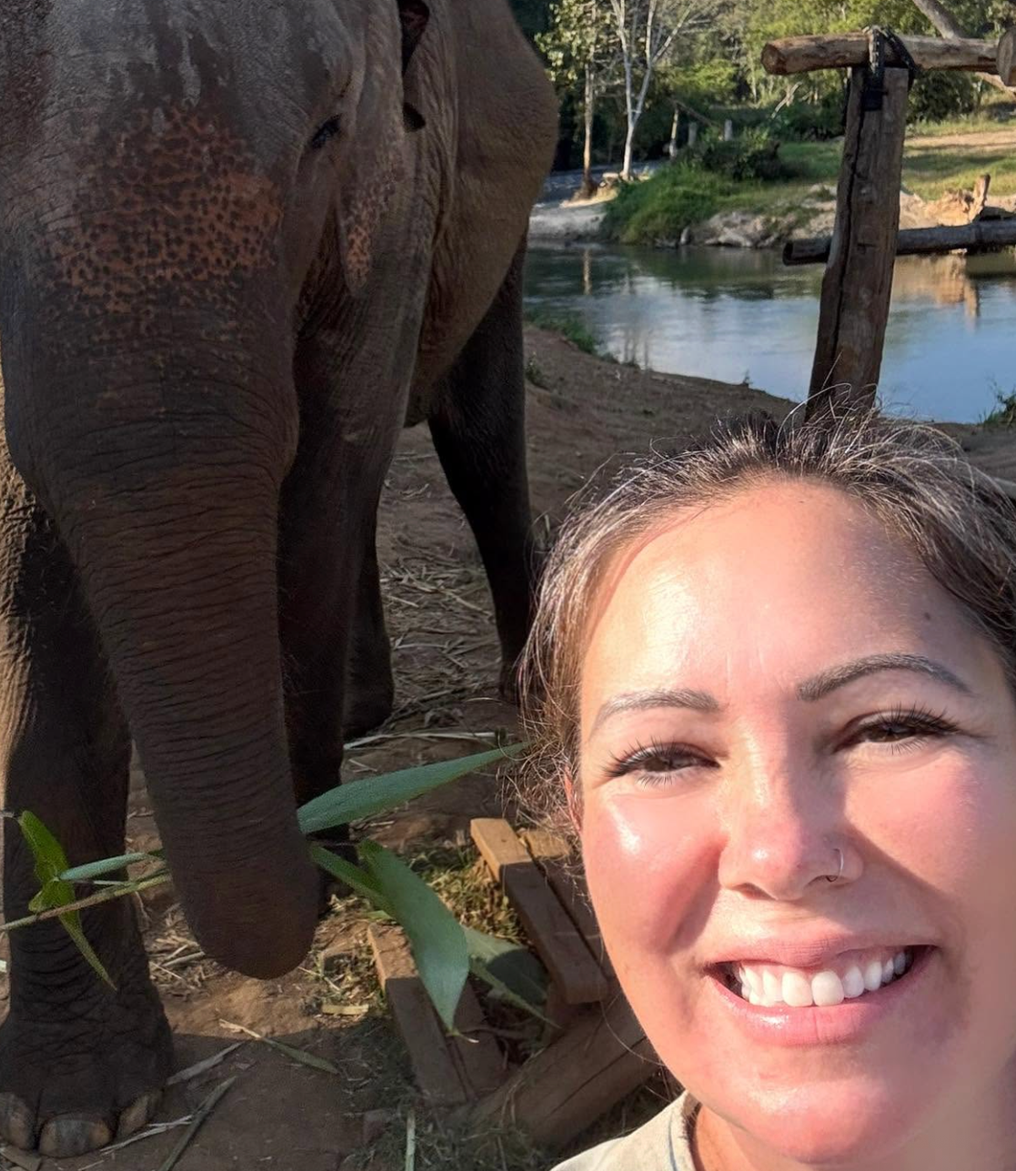Sabrina smiling beside a rescued elephant by a river in Thailand